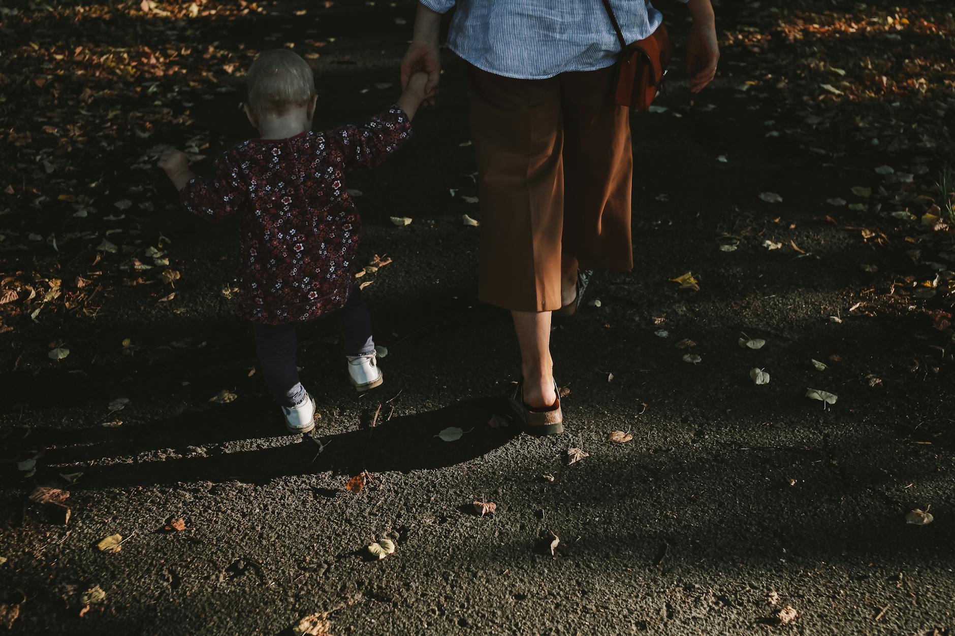 Mama z przedszkolakiem idą za ręce jesienną alejką pełną liści