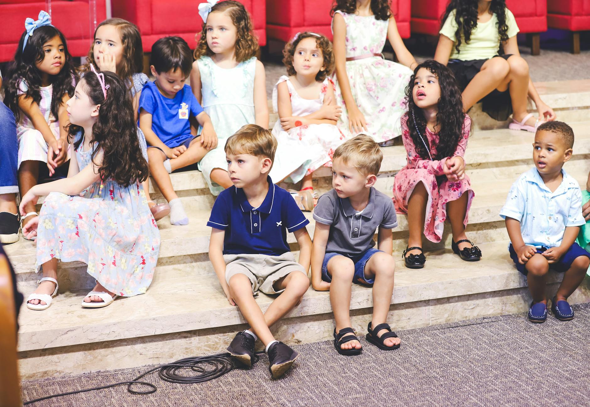 Przedszkolaki w kolorowych ubraniach siedzą na schodach podczas zajęć