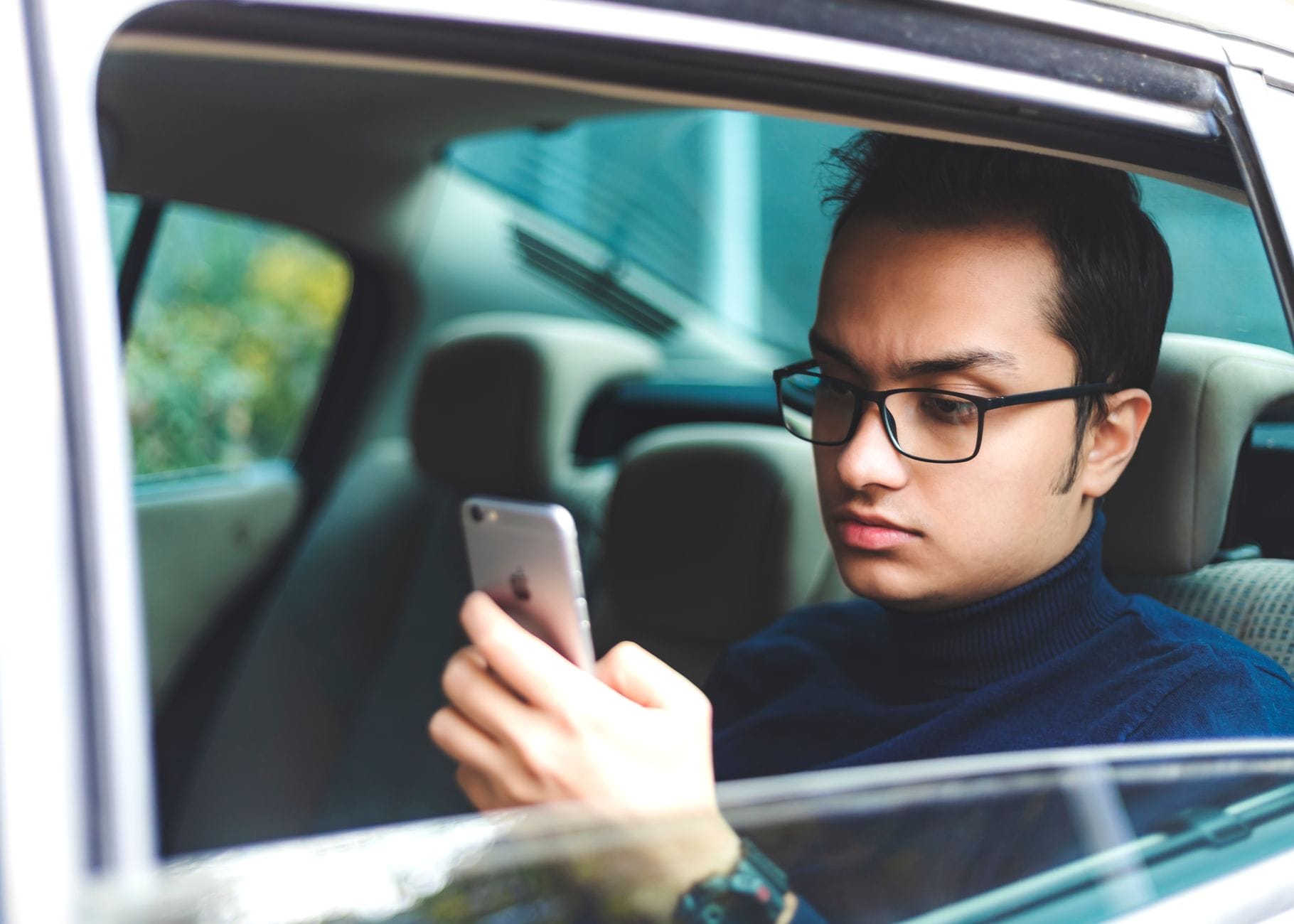 Młody mężczyzna w okularach sprawdza ofertę auta na smartfonie w samochodzie