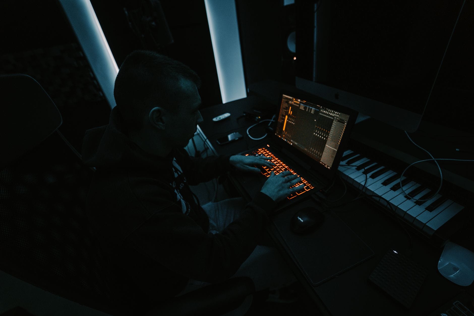 Producent muzyczny komponuje utwór w przyciemnionym studiu z laptopem i klawiatu